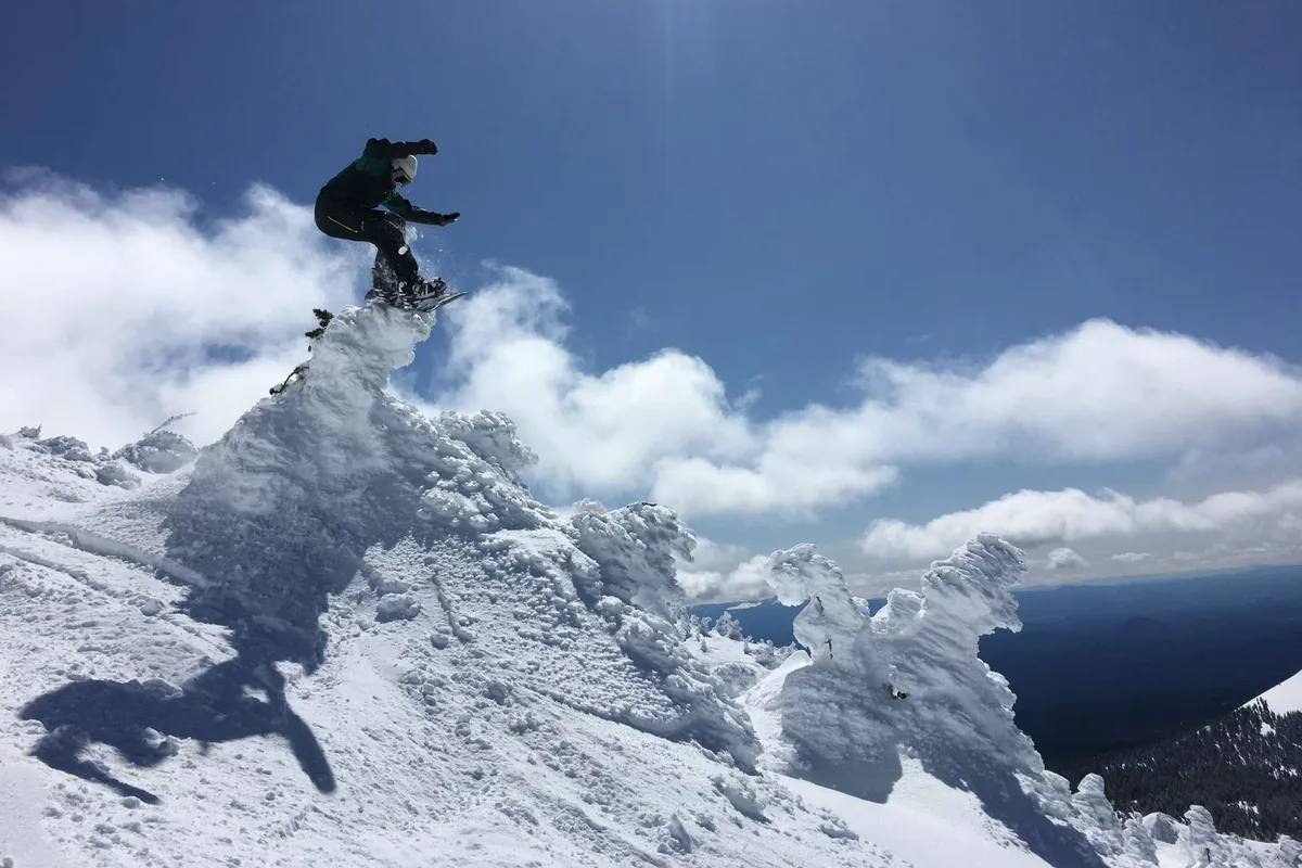 A snowboarder leaps off a snowy peak into the air, surrounded by dramatic clouds and pristine white slopes. The action shot conveys the adrenaline and fun of mountain sports in winter.