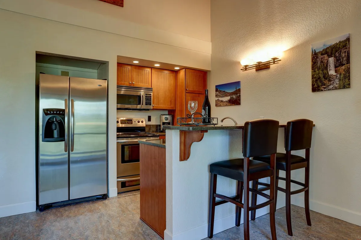 A modern kitchen scene with a spacious island, bar stools, stainless steel appliances, and decorative wall art. The setting is inviting for cooking, casual dining, and entertaining, with a cozy, welcoming atmosphere.