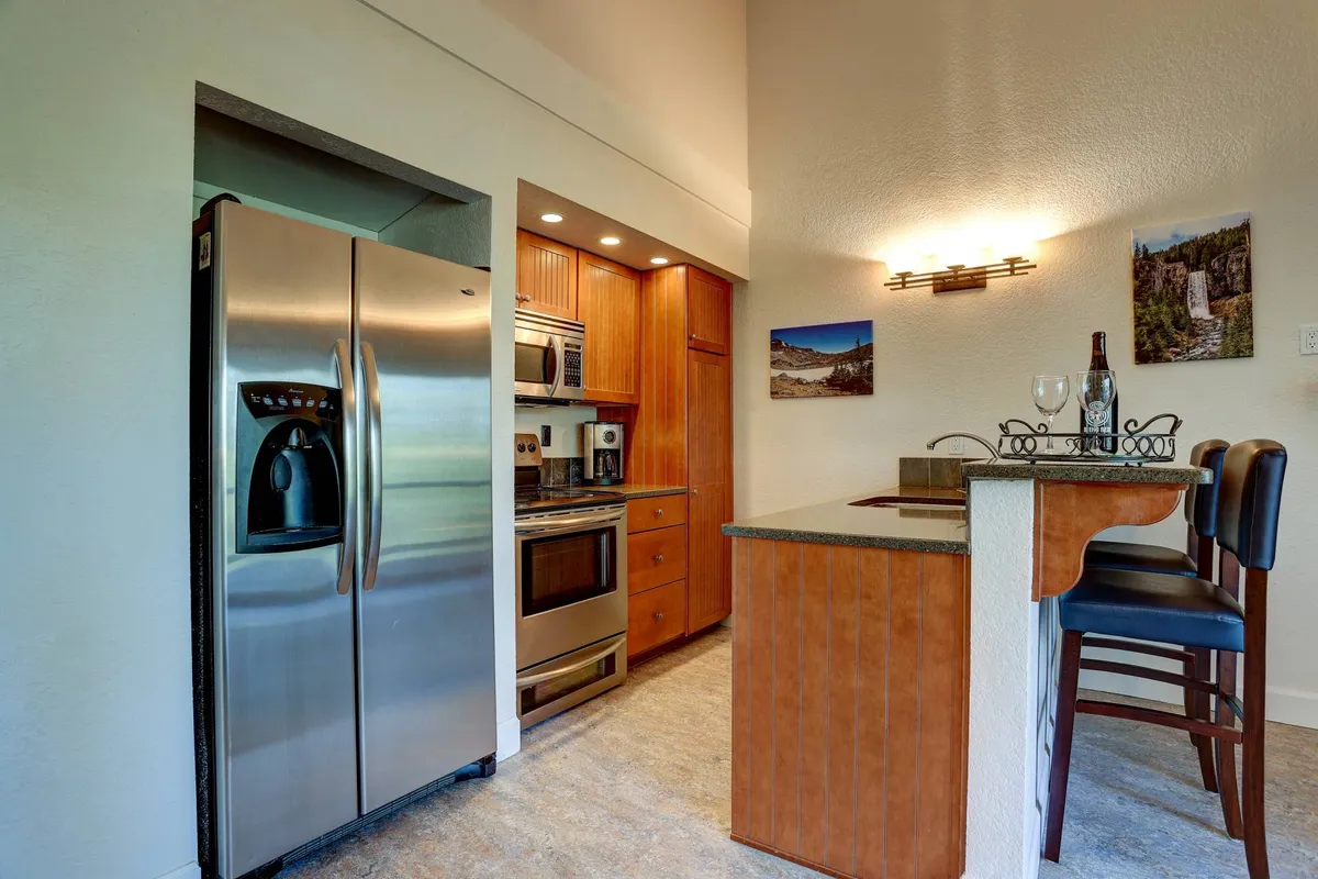 The modern kitchen showcases stainless steel appliances, wood cabinetry, and a kitchen island with seating, hinting at opportunities for entertaining, casual meals, or sampling local culinary finds brought back from Bend’s eateries and markets.