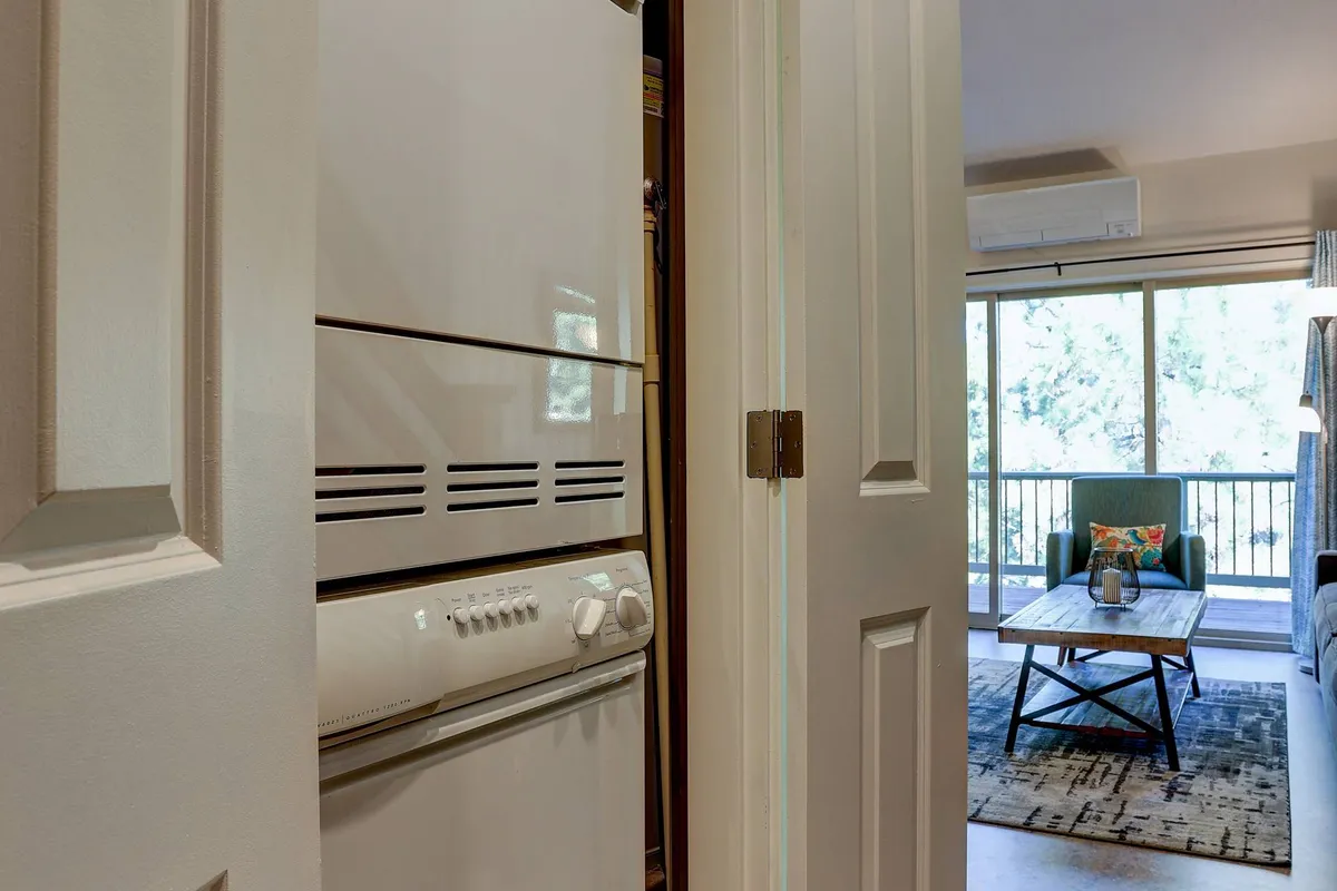 A view from the kitchen shows modern appliances, a cozy living area, and a coffee table by a window letting in natural light. The scene feels lively, welcoming, and ready for shared moments.