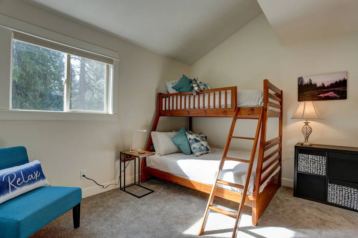 This image showcases a cozy bedroom with a bunk bed, accent chair, decorative pillow, lamp, and nightstand. The space looks inviting and perfectly suited for families or friends who value comfort and privacy.